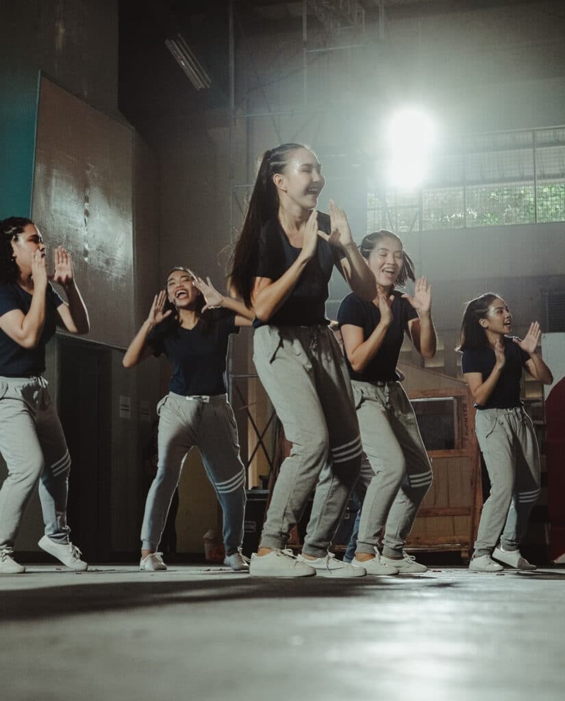 En gruppe unge kvinder danser energisk i et lagerlokale.